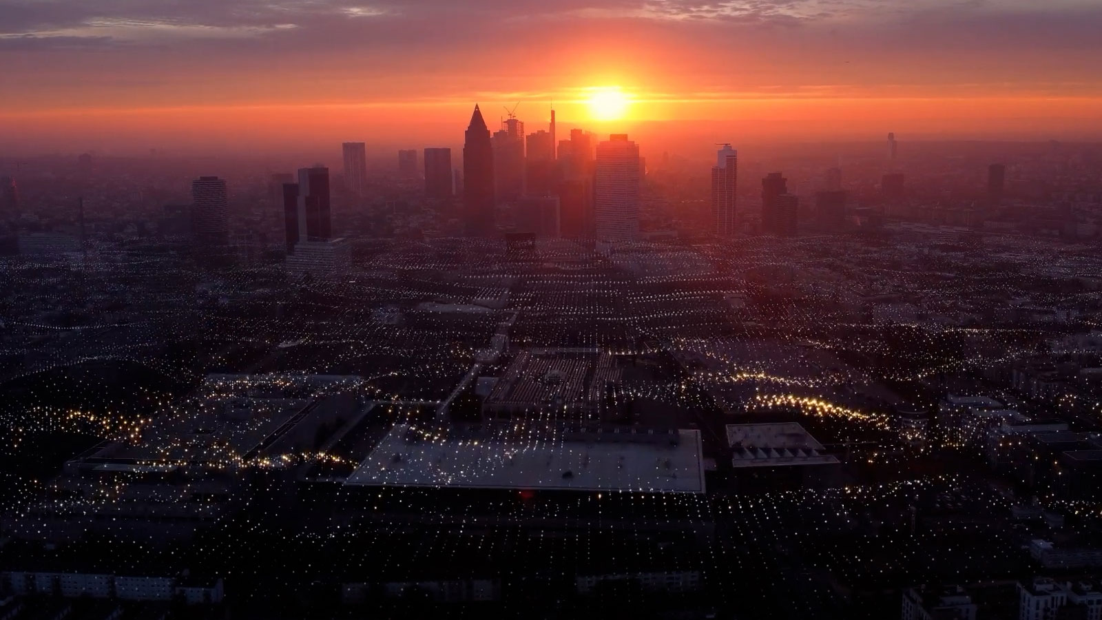 手前全体にわたって輝く光が密につながっている都市の景観に沈む夕日